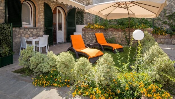 An outdoor seating area with stone walls, a stone staircase, and a garden with yellow flowers. - Apartment Lucia (Vico Equense)