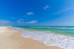 A beach with clear blue water, sandy shore, and a pier in the distance. - Beachfront Bliss @ Gulf House 303, Sea South Properties (Gulf Shores)