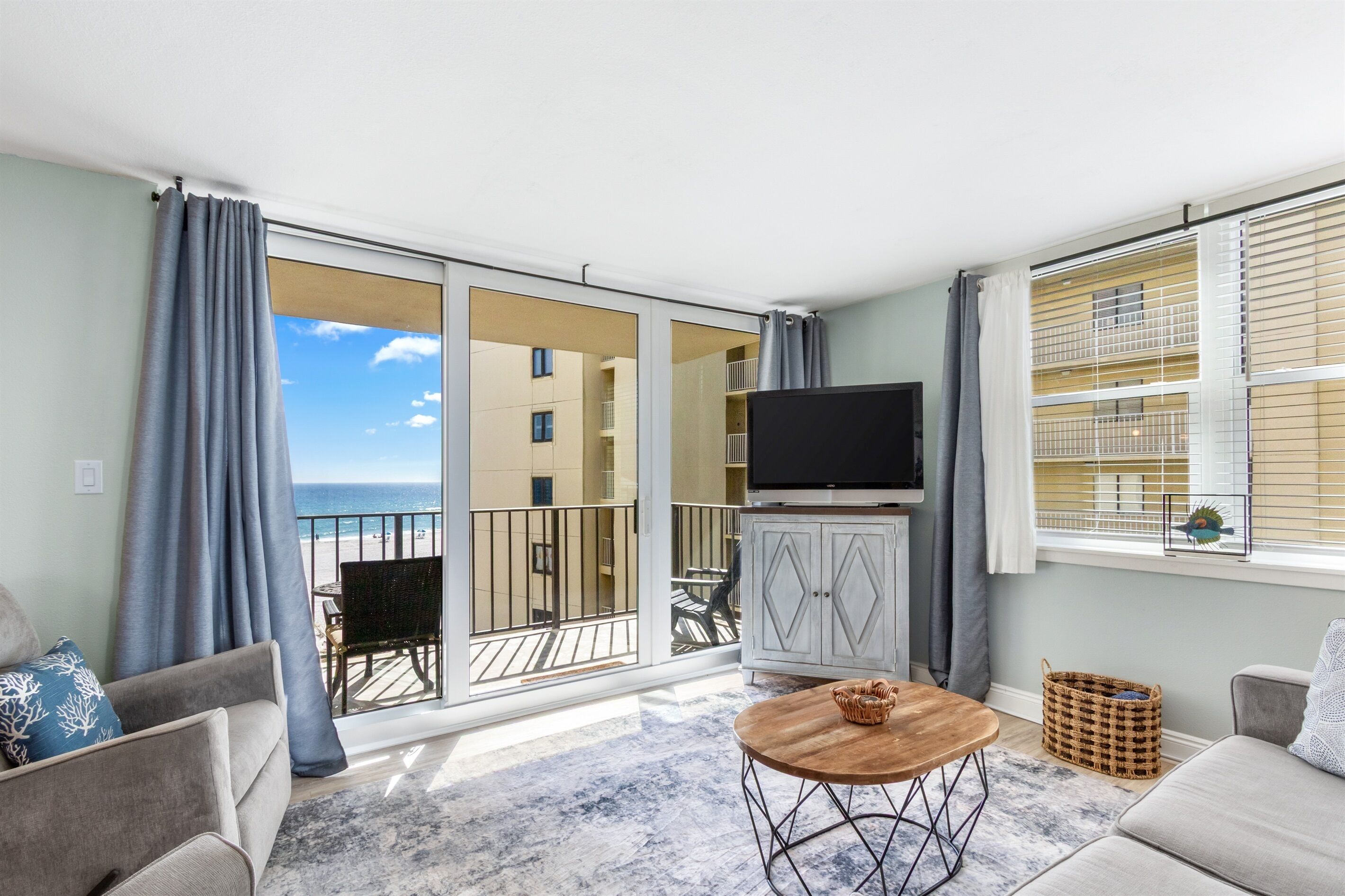A living room with a large sliding glass door to a balcony, a flat-screen TV, and a round wooden coffee table.