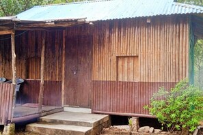 A rustic wooden building with a corrugated metal roof, a small porch with steps, and a door. - Hep Homestay (ML)