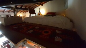 Een slaapkamer met een groot bed, een stoel, een tafel met een lamp en een plafond met zichtbare balken.