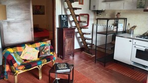 Een knus leefruimte met een bank, een klein tafeltje, een trap, een kitchenette en een deur naar een andere kamer.