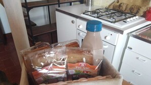 Een keuken met een gasfornuis, een koelkast en een rieten mand met verpakte etenswaren.