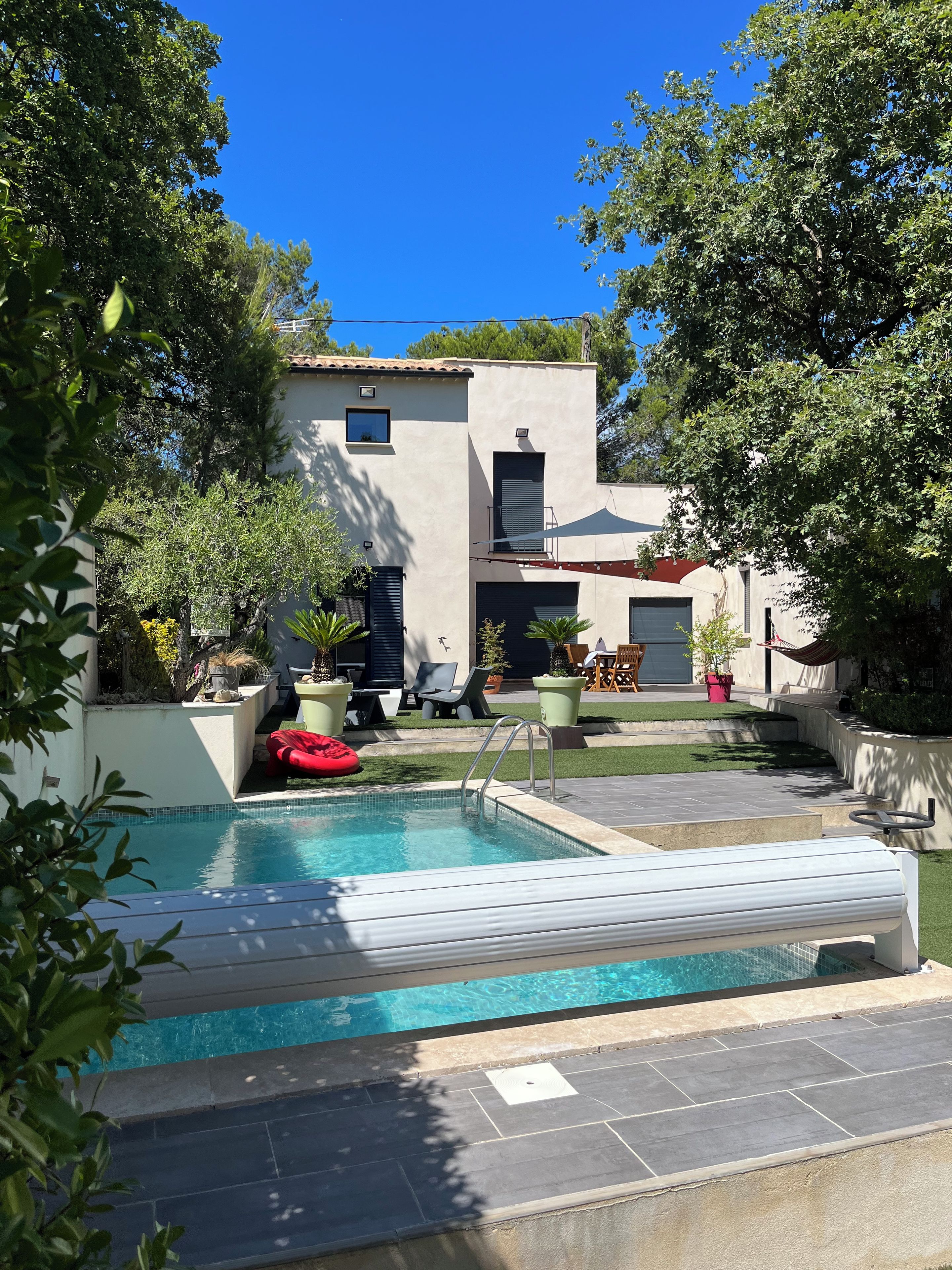 Une piscine dotée d’une terrasse carrelée, entourée de plantes en pot et de mobilier d’extérieur.