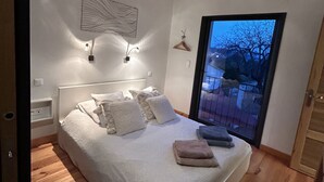 A bedroom with a bed, bedside lamps, a view through a window, and a wooden floor.