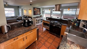 Una cocina con horno integrado, cafetera y estufa. Hay una zona de comedor con sofá y ventana.