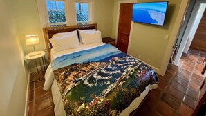 Un dormitorio con una cama, un televisor en la pared y una ventana.