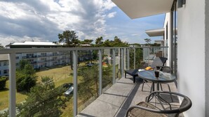 A balcony with a glass railing, a table with chairs, and a view of a residential area with trees and buildings. - Air-conditioned Studio | Balcony, Gym and 50 m to the Beach (Mielno)