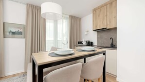 A modern kitchen with wooden cabinets, a dining table with two chairs, and a hanging light fixture. - Air-conditioned Studio | Balcony, Gym and 50 m to the Beach (Mielno)
