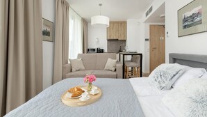 A modern hotel room with a bed, a breakfast tray, a sofa, a dining area, and a kitchen. - Air-conditioned Studio | Balcony, Gym and 50 m to the Beach (Mielno)