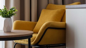 Un sillón amarillo con estructura negra, un jarrón blanco con plantas verdes y una mesa redonda de madera.