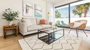 A modern living room with a sofa, coffee table, and a view of palm trees through large windows.
