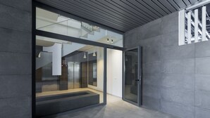 A modern building entrance with a glass door, a staircase leading to an upper level, and a tiled floor.
