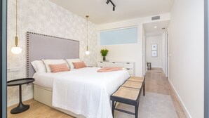A modern bedroom with a large bed, bedside tables, a bench, and a window.