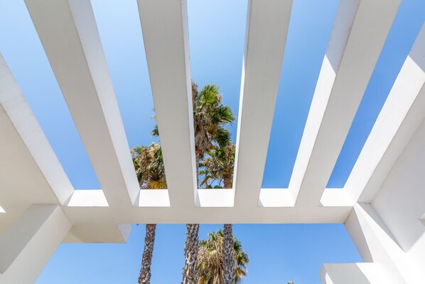 A white pergola structure with a clear blue sky and palm trees in the background.