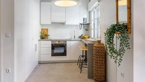Eine moderne Küche mit weißen Schränken, einem eingebauten Backofen, einer Hängeleuchte und einem großen Fenster.