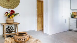 Ein modernes Interieur mit einer Holztür, einem gewebten Wandbehang, einem kleinen Holztisch mit Blumen in einer Vase und einem rustikalen Teppich.