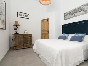 Un dormitorio con una cama, un armario de madera, un reloj en la pared, una puerta y un cuadro enmarcado.