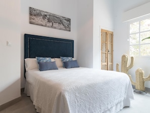 A bedroom with a bed, a headboard, a window, and a cactus plant.