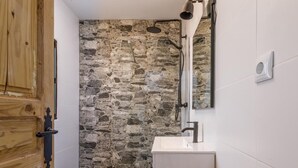Ein Badezimmer mit Steinwand, Toilette in Weiß, Dusche mit Handbrause und Holztür.
