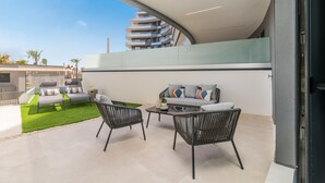 Een modern buitenterras met een gebogen dak, een loungeset, twee fauteuils en een kleine tafel.