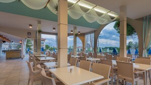 Un amplio espacio exterior para comer con varias mesas y sillas, grandes ventanales que ofrecen vistas del paisaje circundante y un techo con diseño ondulado.
