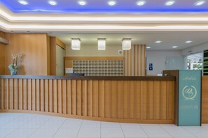 Mostrador de recepción de hotel con diseño de paneles de madera, una barra de recepción y un letrero con el nombre del hotel.