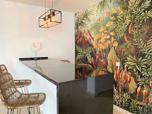 A modern kitchen with a black countertop, wicker chairs, and a unique wall mural.