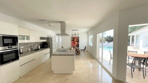 Een moderne keuken met witte kastjes, een centraal eiland en uitzicht op een zwembad.