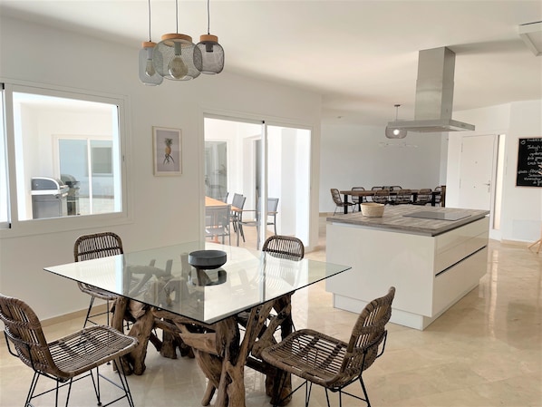 A modern kitchen with a central island, glass dining table, and wicker chairs.