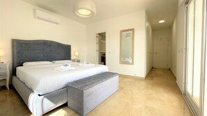 Een moderne slaapkamer met een groot bed, nachtkastjes, een bankje, een plafondlamp en een spiegel.