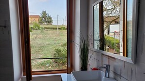 Ein modernes Badezimmer mit einem großen Fenster, einem weißen Waschbecken und einem Spiegel.