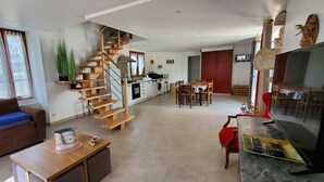 Ein modernes Wohnzimmer mit einer Holztreppe, einem Essbereich und einer Küche im Hintergrund.
