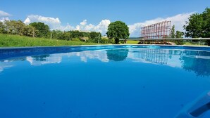 Ein klares, blaues Schwimmbecken mit einer gefliesten Kante, umgeben von einer Rasenfläche und Bäumen.