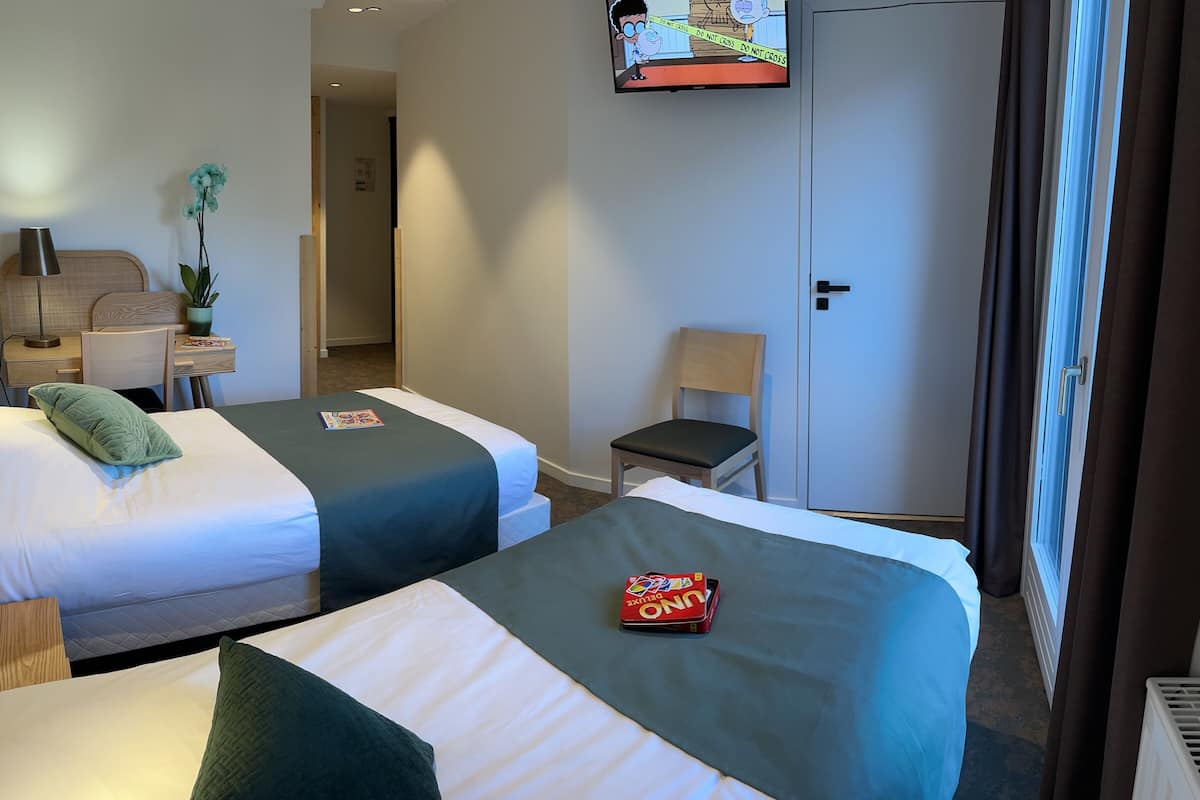 Ein Hotelzimmer mit zwei Betten, einem Schreibtisch, einem Stuhl, einem Fernseher und einem Kleiderschrank.