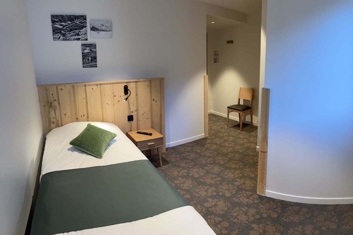 Ein Hotelzimmer mit einem Bett, einem kleinen Tisch mit Fernbedienung, einem Sessel und einem Fenster mit Orchidee.