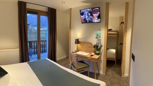 Habitación de hotel con cama, escritorio con silla, televisión y vista a las montañas por la ventana.