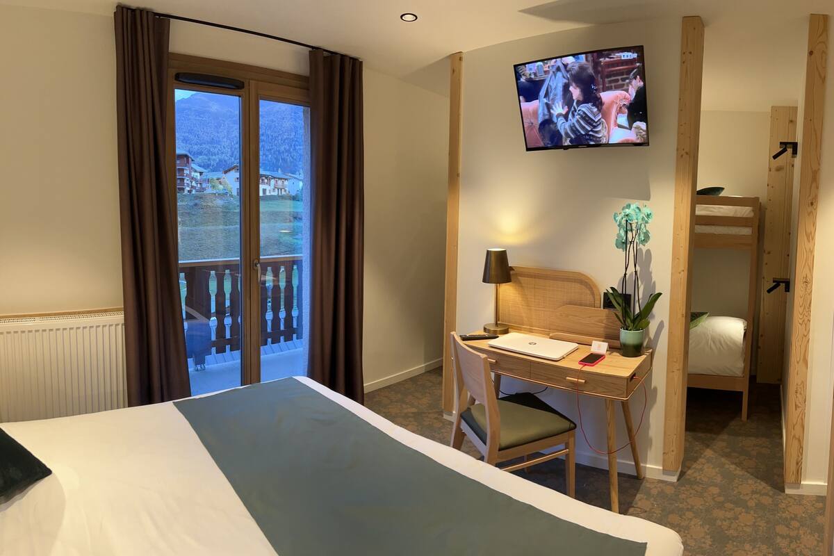 Ein Hotelzimmer mit Bett, Schreibtisch mit Stuhl, Fernseher und Blick auf die Berge durch das Fenster.