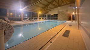 Una piscina interior con sillones de descanso y suelo de baldosas.
