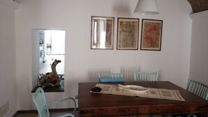 A dining area with a wooden table, light blue chairs, and a hanging light fixture. There are three framed artworks on the wall.