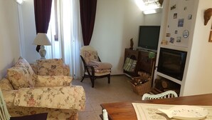 A living room with a sofa, armchair, wooden dining table, TV, and wall decorations.