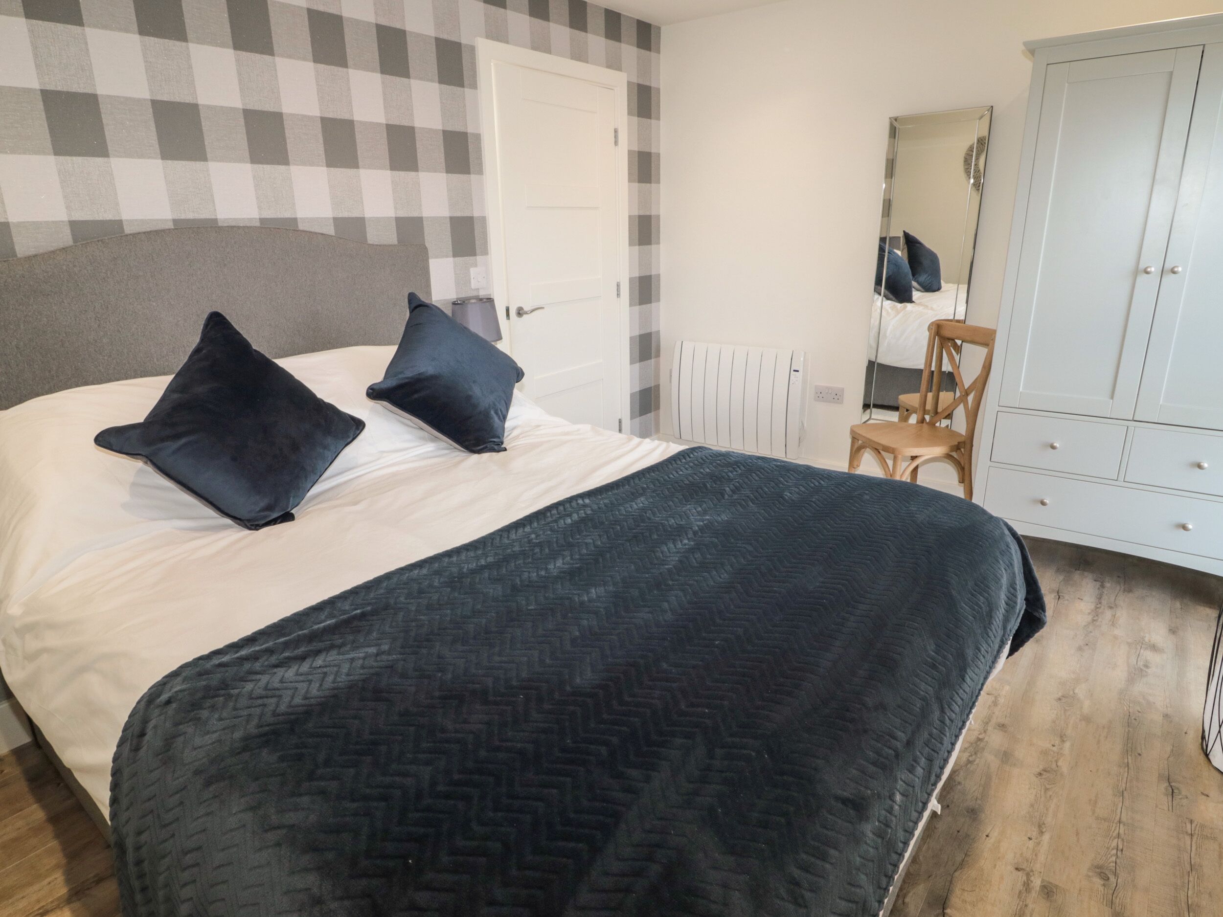 A bedroom with a bed, two pillows, a dresser, a chair, and a radiator.