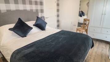 A bedroom with a bed, two pillows, a dresser, a chair, and a radiator.
