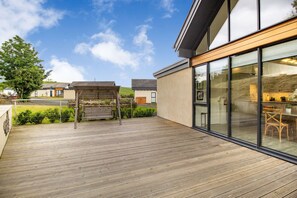 Ein modernes Haus mit Holzterrasse, großen Glasfenstern und Blick auf die Umgebung.