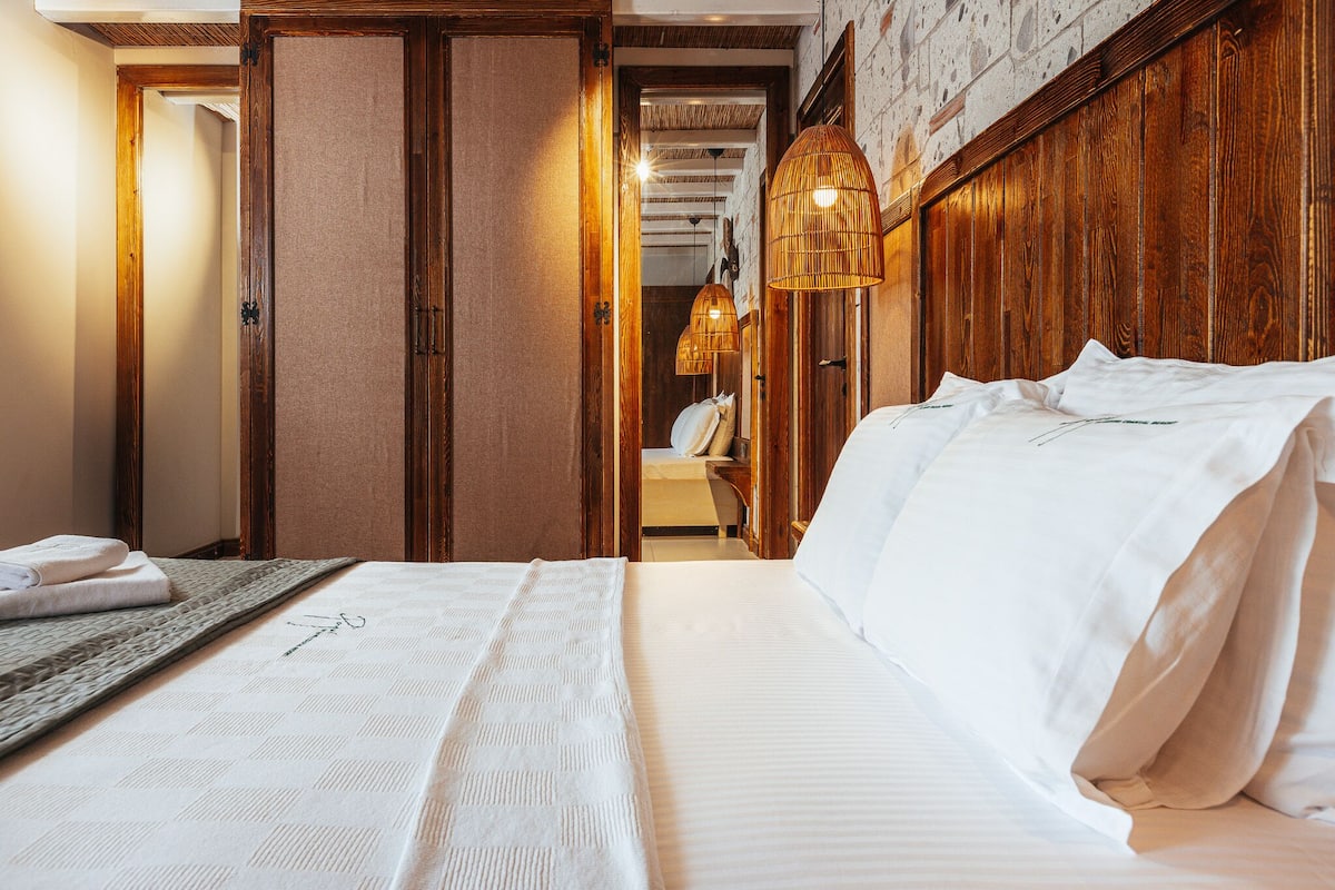 A hotel room with a large bed, wooden headboard, and a view of a hallway with a wooden door and a mirror.