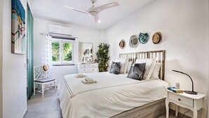 A bedroom with a bed, a nightstand, a chair, a ceiling fan, and a window with curtains.