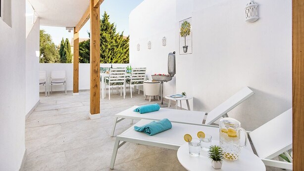 A modern outdoor patio with white furniture, a grill, and a small table with drinks.