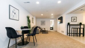 A modern living room with a dining area, a flat-screen TV mounted on the wall, and a small side table with plants. - Cozy 2bd |10 min to Downtown Denver | Fast Wifi (Denver)