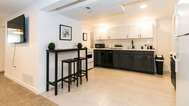 A modern kitchen with white cabinets, a black countertop, and a built-in oven. There are two black bar stools and a small potted plant on the counter. - Cozy 2bd |10 min to Downtown Denver | Fast Wifi (Denver)
