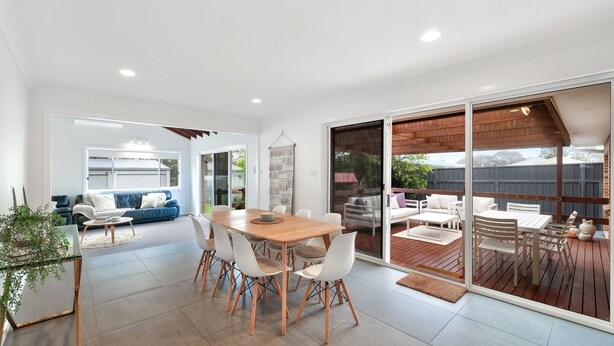 A modern home interior with a dining area, a living room with a blue sofa, and a patio with outdoor furniture.